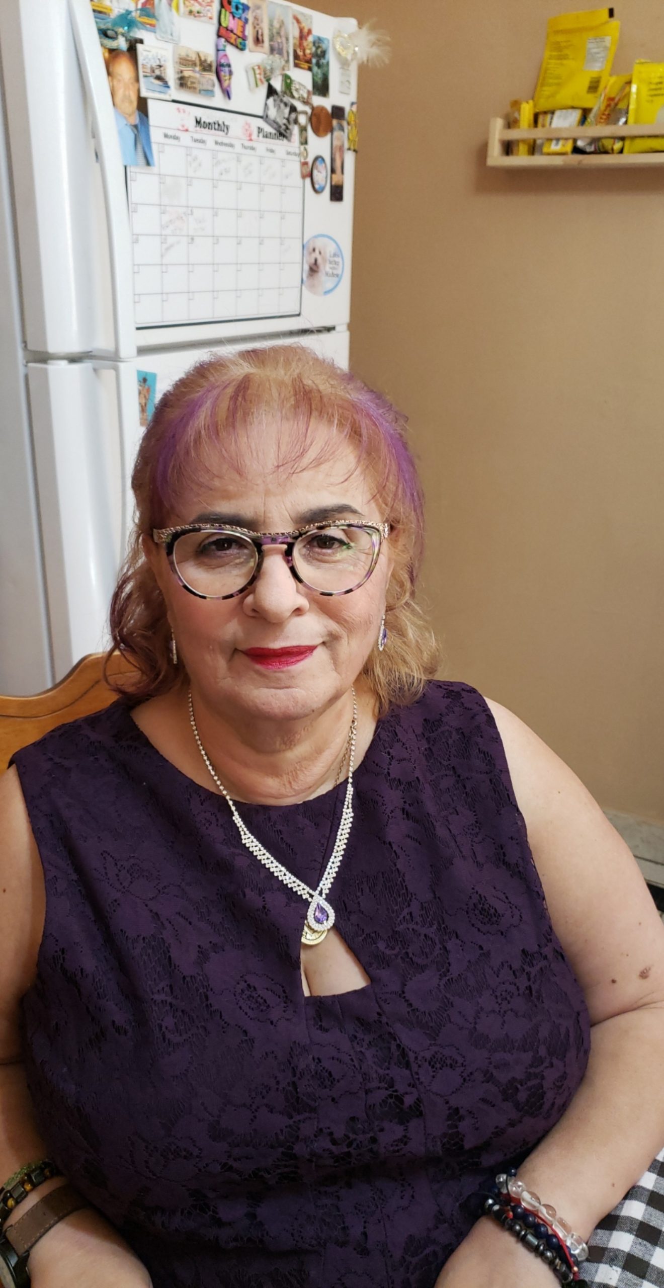 Woman with purple hair and a purple dress sitting in a kitchen